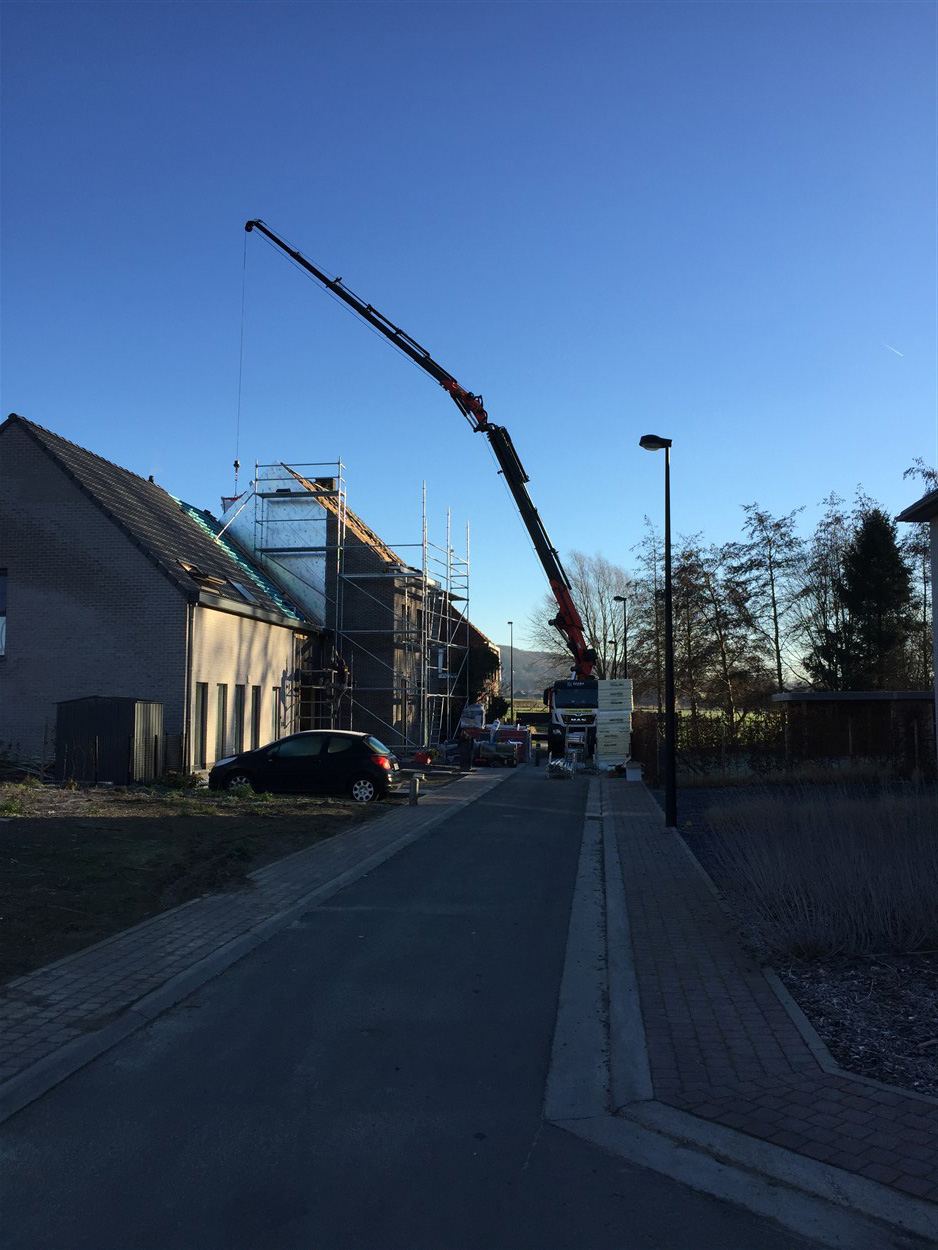 Kraanwagen in een residentiele straat hijst steigermateriaal naar een dak in renovatie