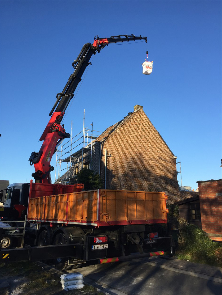 Kraanwagen met volledig uitgeschoven giek hijst bouwmateriaal op grote hoogte