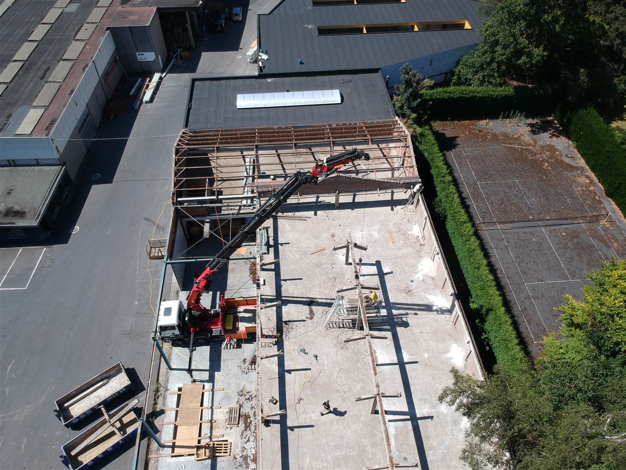 Luchtfoto van een kraan die een stalen dakconstructie plaatst op een plat dak van een industrieel gebouw