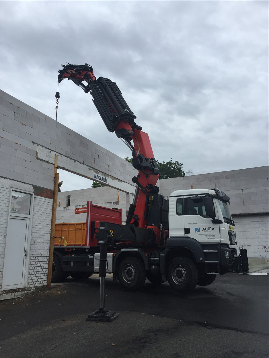 DAKRA-kraanwagen met cabine geparkeerd bij een magazijngebouw, arm hijst last richting muuropening